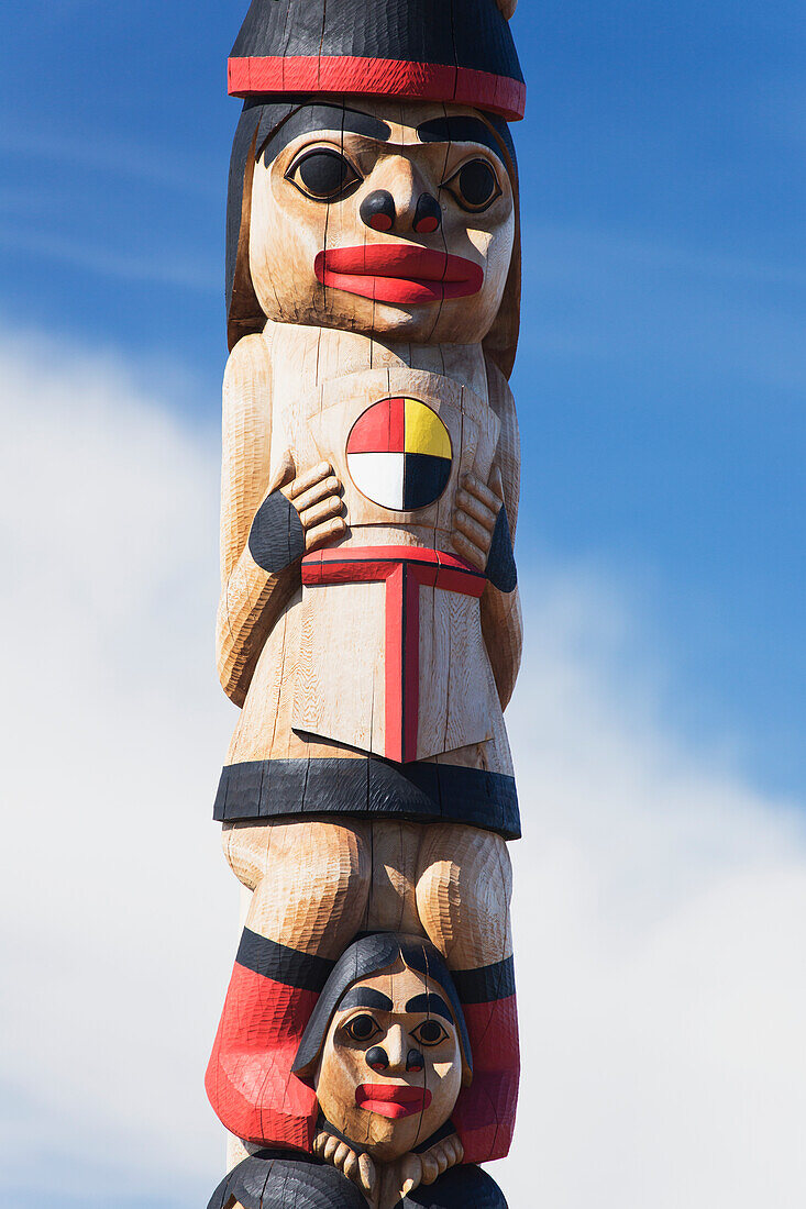 'Human figures carved and painted on a wooden totem pole against a blue sky; Whitehorse, Yukon, Canada'