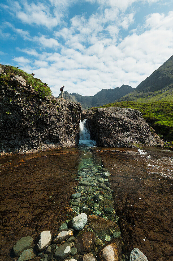 'Man looking at small waterfall near the Fairy Pools in Coire na Creiche, Black Cuillin; Isle of Skye, Scotland'