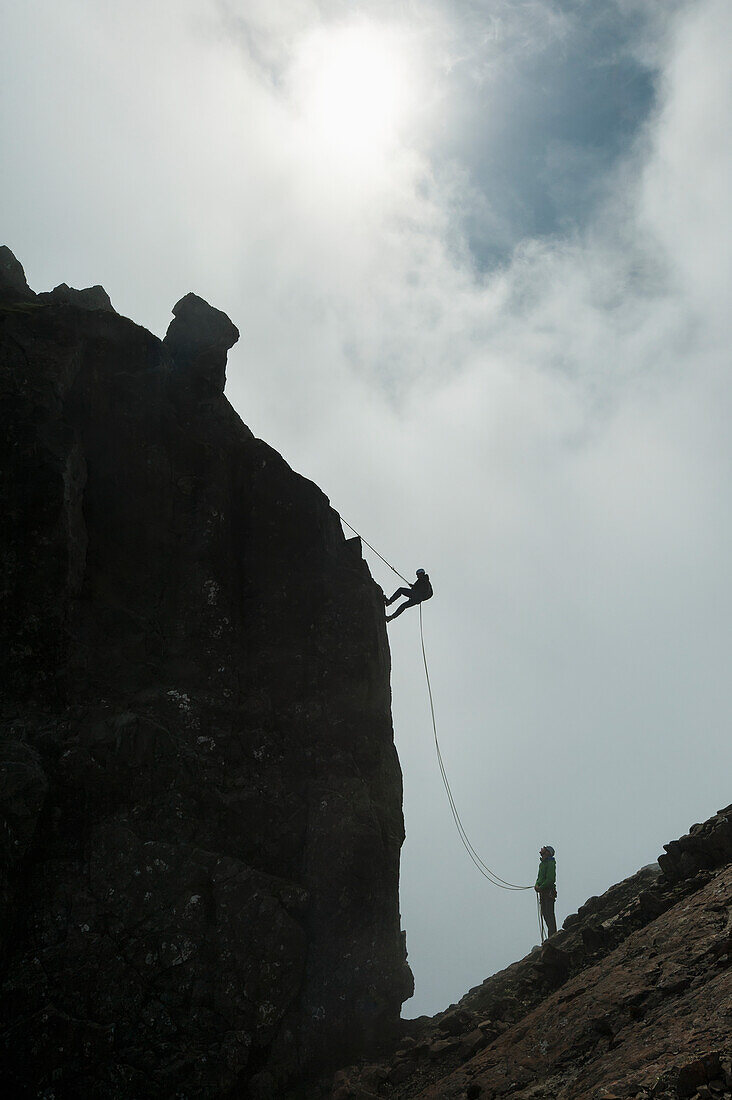 'Silhouette of people abseilling off the Inaccessible Pinnacle at the summit of Sgurr Dearg; Isle of Skye, Scotland'