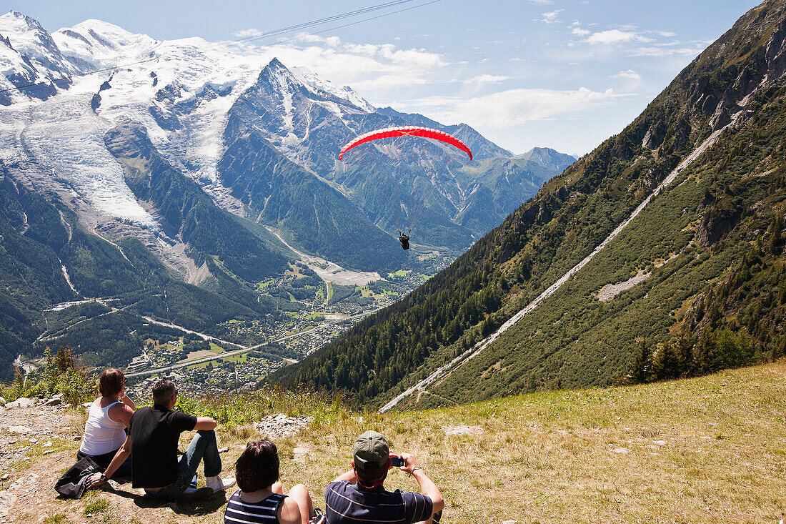 'Tourists watching paraglider flight at take-off point above Chamonix-Mont Blanc valley, with Mont Blanc mountain in background; France'