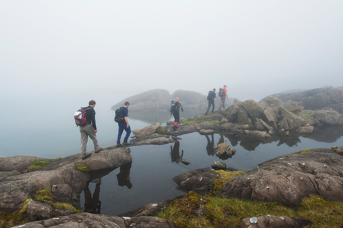 'Hikers walking past small loch in the mist below Sgurr Alasdair in the Black Cuillins; Isle of Skye, Scotland'