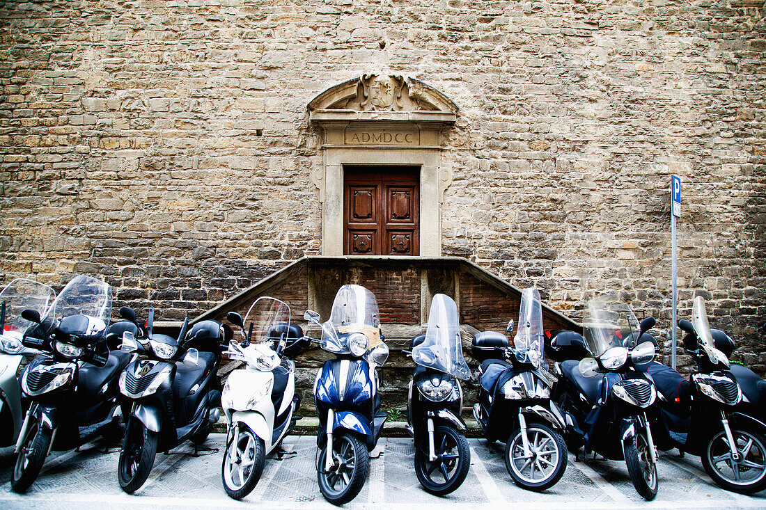 'Motorcycles parked in a row outside the entrance to a stone building; Florence, Tuscany, Italy'