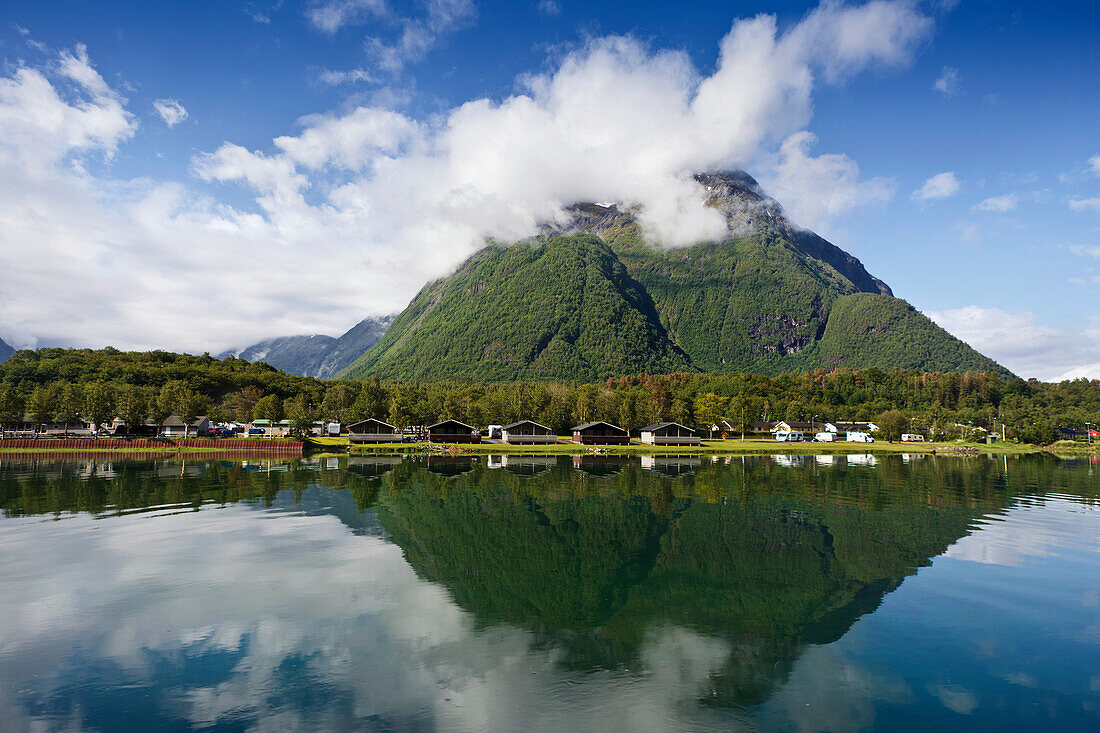'A green mountain with the peak covered in cloud reflected in the tranquil water; Andalsnes, Rauma, Norway'