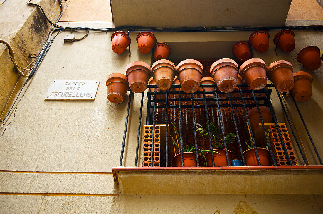 'Ceramic flower pots hanging on the edge of a metal railing on a residential balcony; Barcelona, Spain'