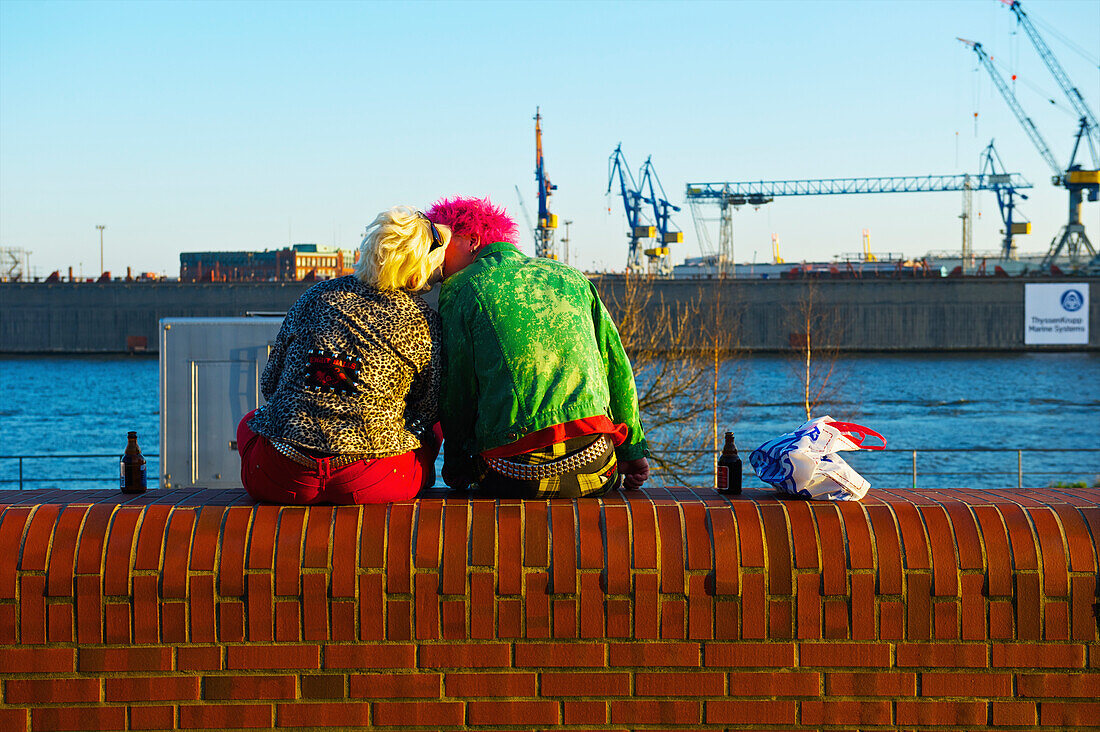 'A trendy couple sitting on a ledge by the river kissing; Hamburg, Germany'