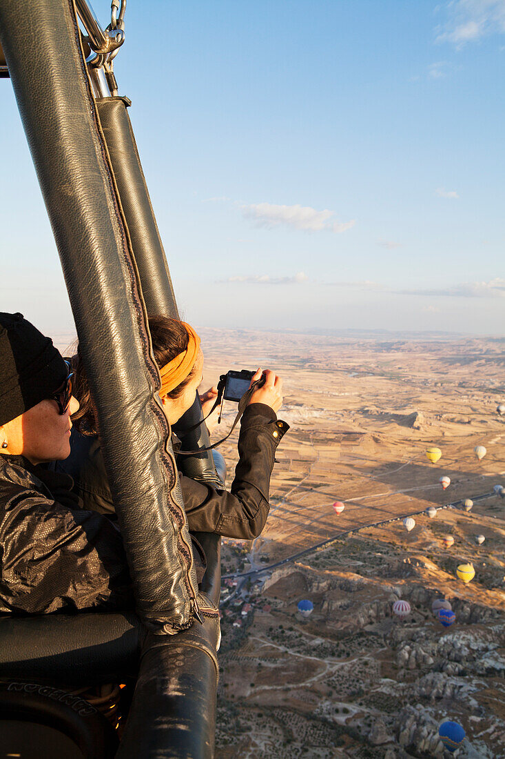 'Tourists in a hot air balloon taking pictures of the view below; Cappadocia, Turkey'