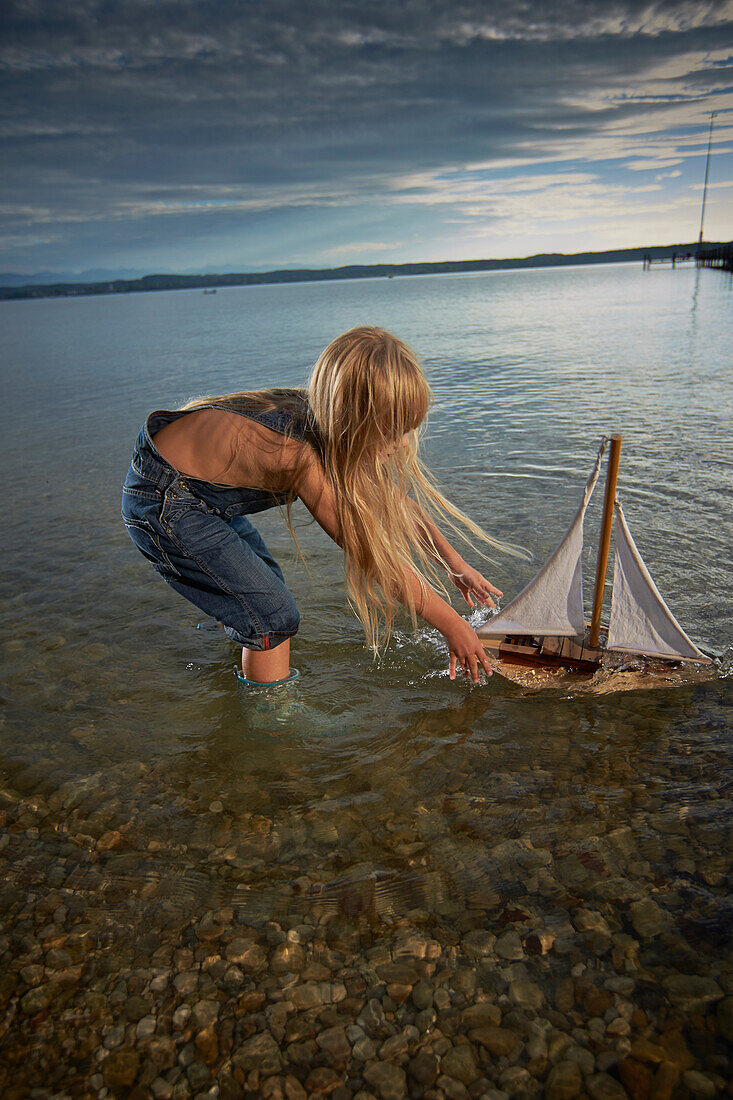 Girl with a toy sailboat in lake Starnberg, Upper Bavaria, Bavaria, Germany