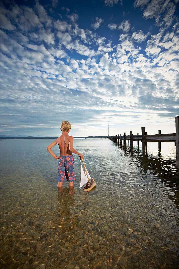 Junge mit einem Spielzeugsegelboot steht im Starnberger See, Oberbayern, Bayern, Deutschland