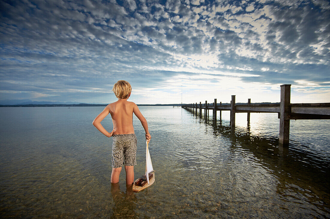Boy with toy sail boat standing in lake Starnberg, Upper Bavaria, Bavaria, Germany