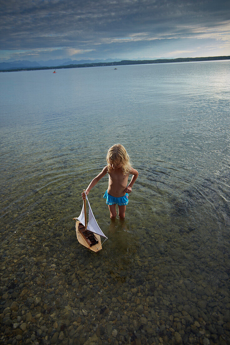 Girl with a toy sailboat in lake Starnberg, Upper Bavaria, Bavaria, Germany