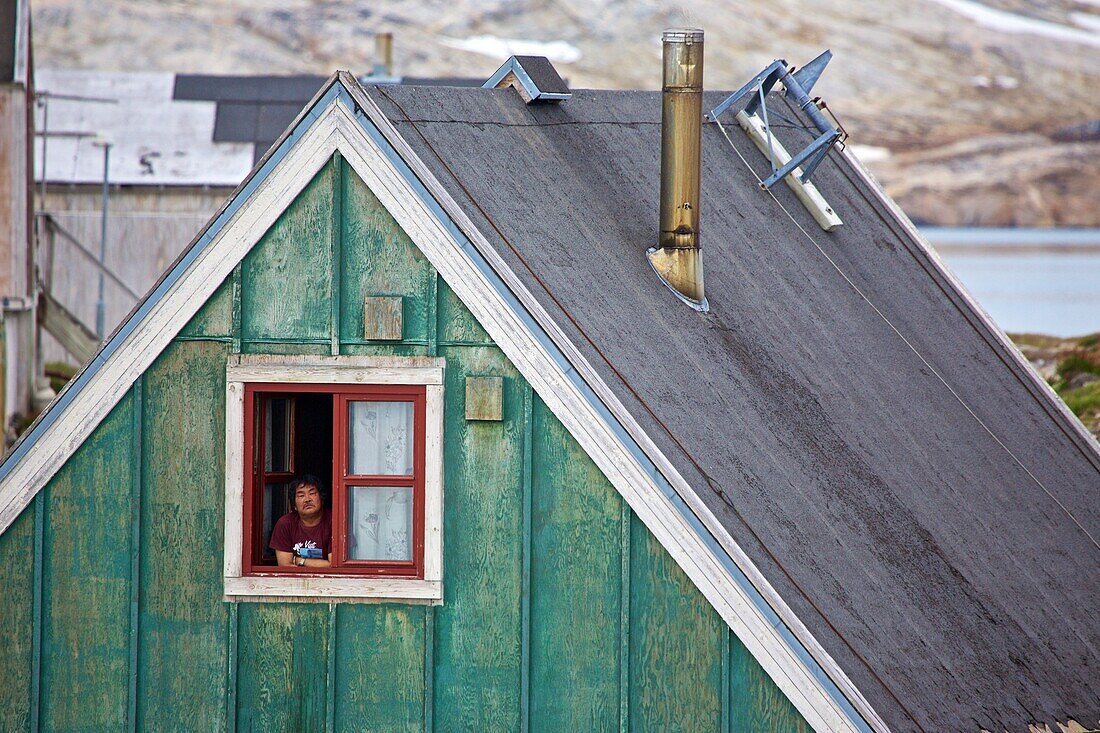Inuk am Fenster eines Hauses in Isortoq, Ostgrönland, Grönland