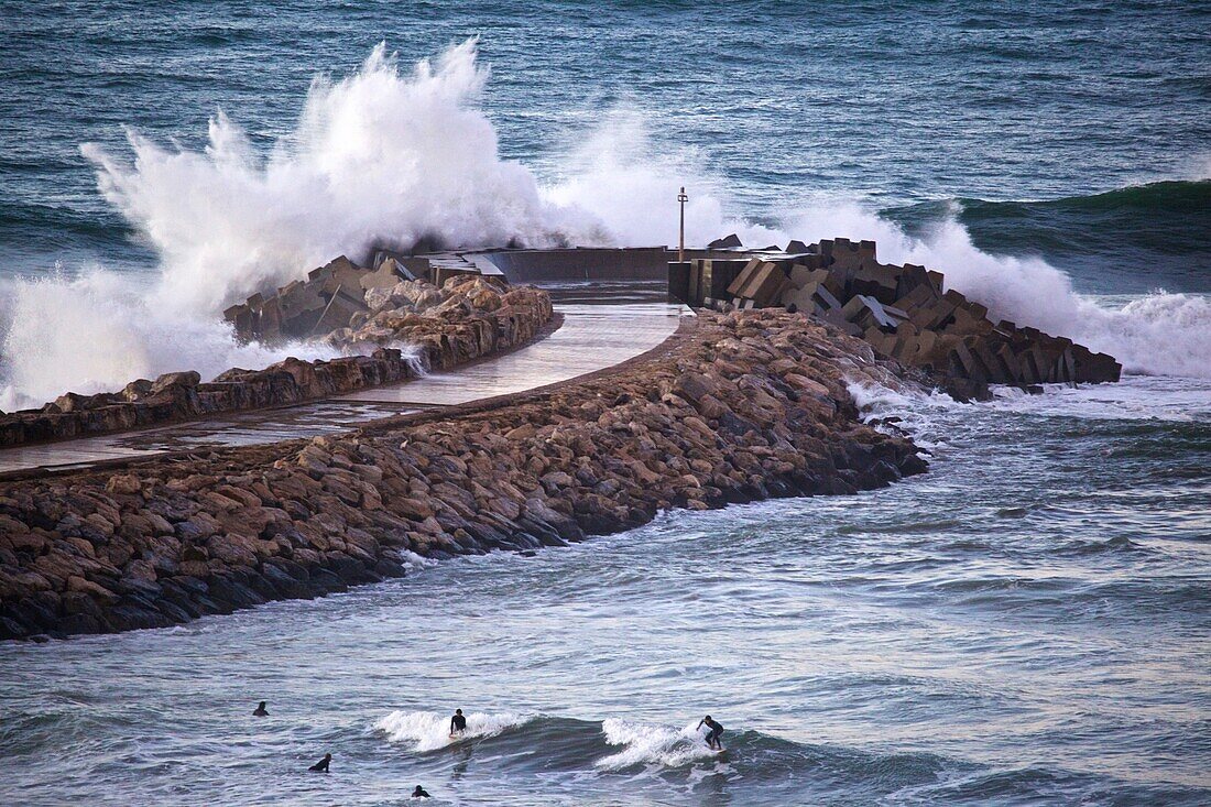 Waves breaking against the port wall of Rabat, with surfers in the harbour basin of Rabat, Marocco