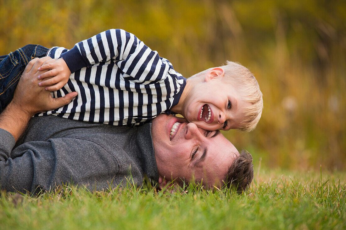 'Father playing with his young son on the grass in a park in autumn; Edmonton, Alberta, Canada'