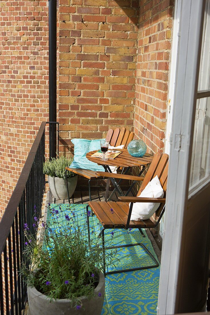 A sunny spot on a balcony in front of a brick facade with wooden chairs and pots of lavender