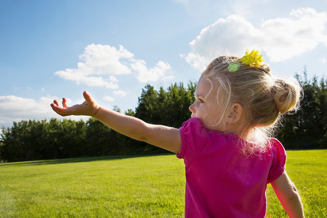 'A young girl reaching up to the sky in a park; St. Albert, Alberta, Canada'