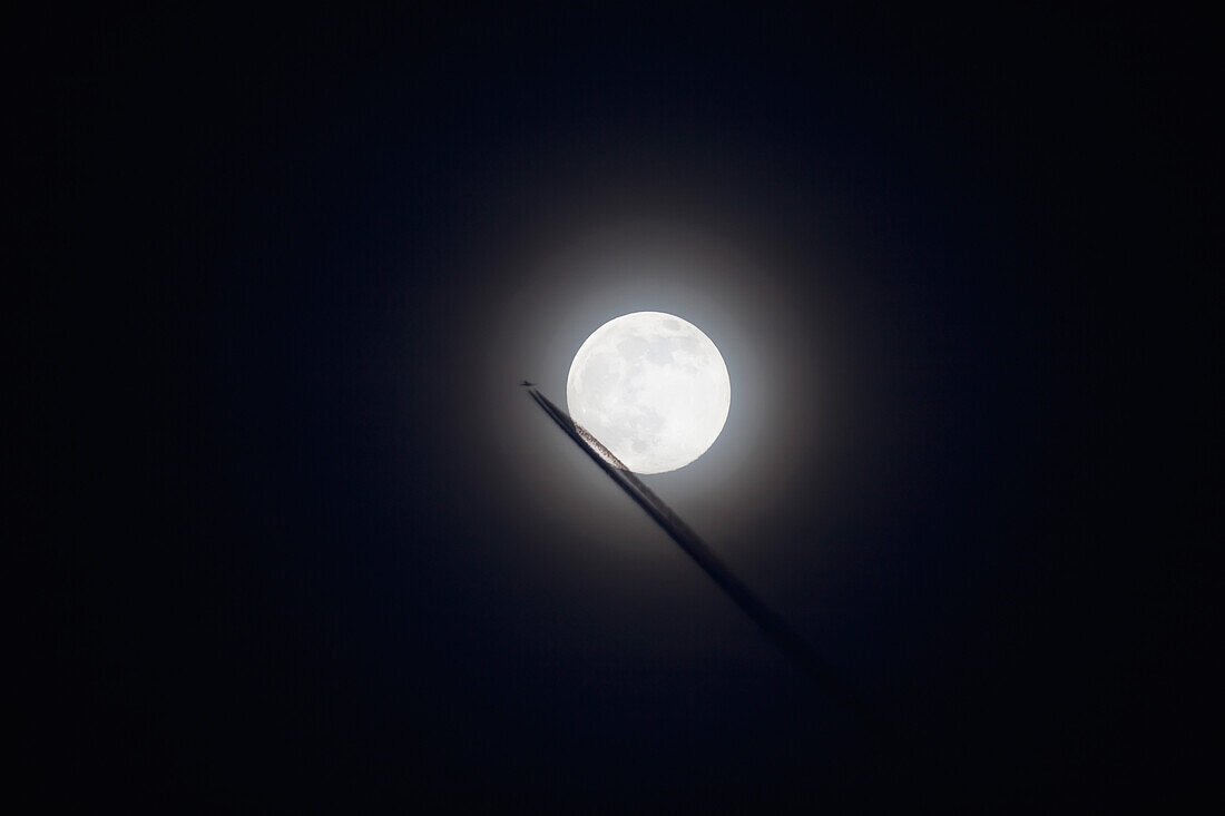 'Commercial jet leaves a vapor trail as it flies past the full moon; Prescott, Arizona, United States of America'