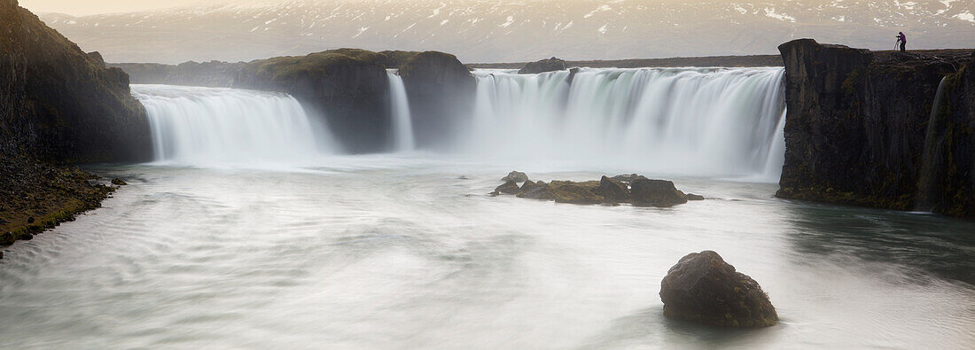 'Panoramic view of Gooafoss waterfall, with photographer standing on edge showing it's scale; Iceland'