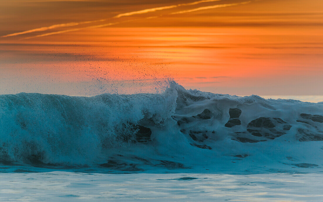 'Waves breaking at the shore with a glowing orange sky at sunset; Tarifa, Cadiz, Andalusia, Spain'