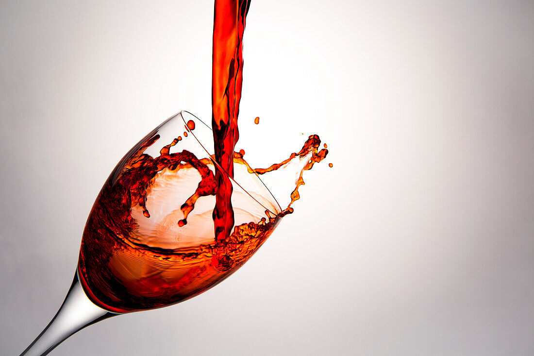 'Close up of red wine being poured into a wine glass and splashing out; Calgary, Alberta, Canada'