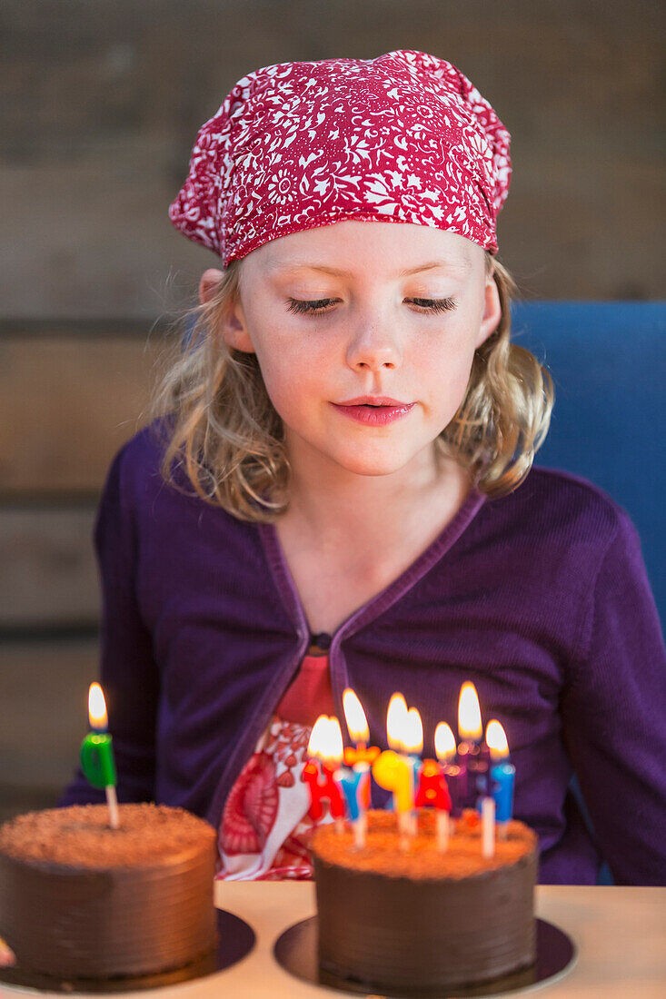 'Young girl wearing red bandana on her head and blowing out the candles of a birthday cake; Anchorage, Alaska, United States of America'