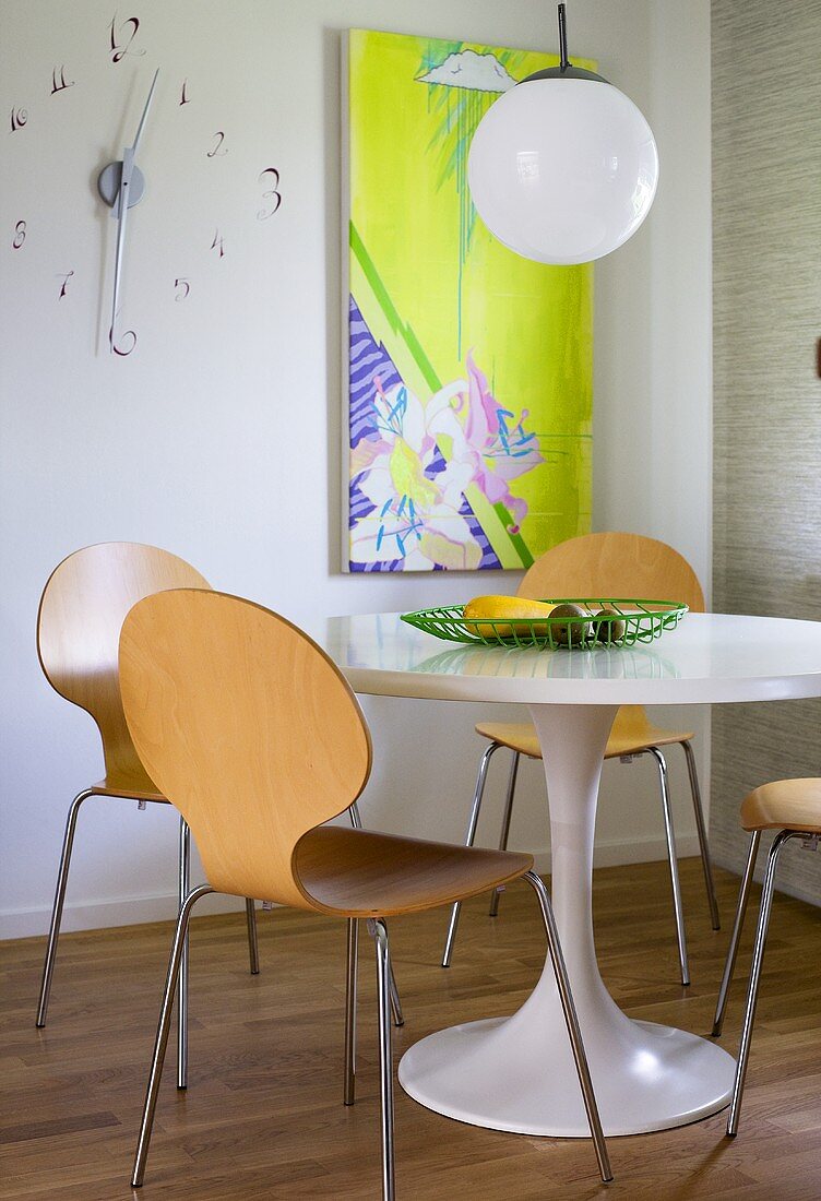 A corner of a dining room - a white table with wooden bucket chairs and a round pendent lamp