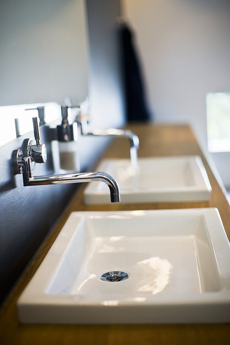 Wall taps above wash basins built into a wooden counter