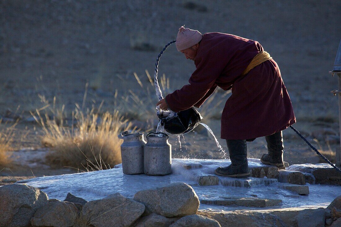 Mönch beim Wasserholen an einem Brunnen im Kloster Amarbuyant im Winter, Mongolei