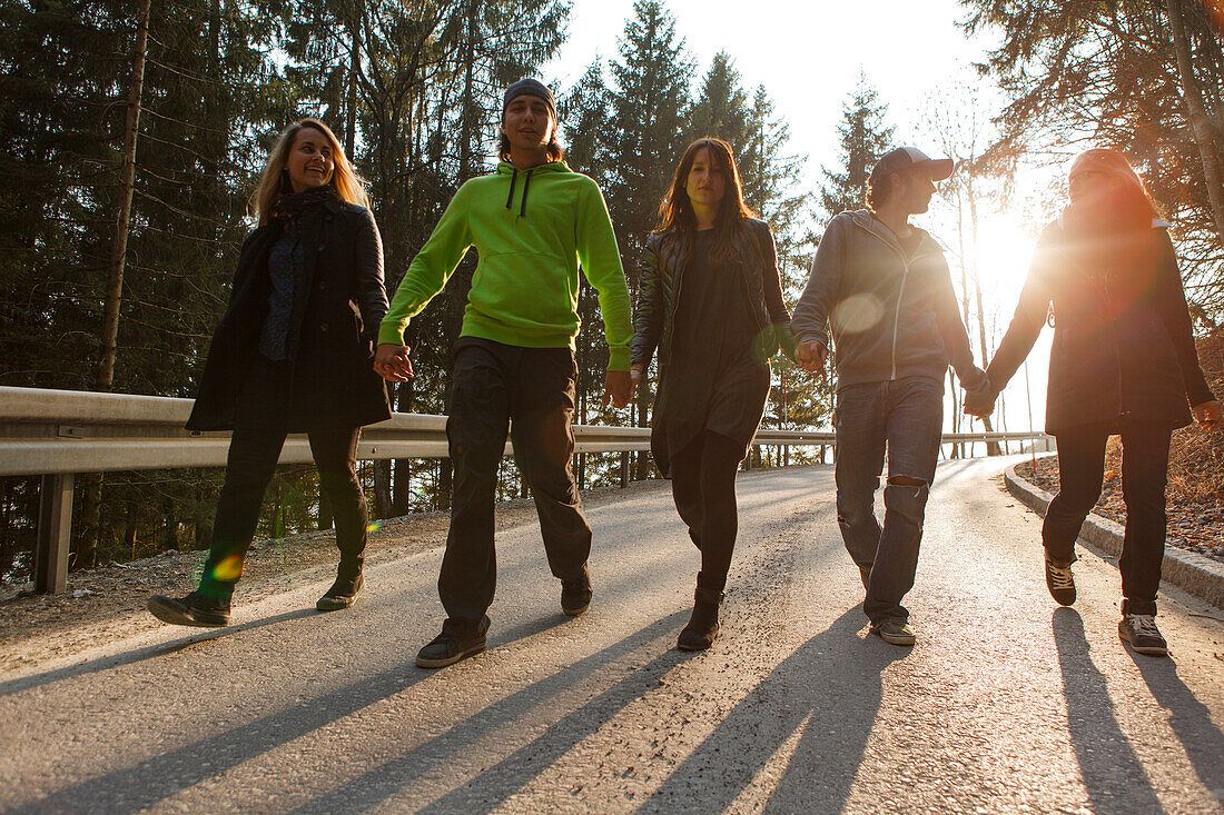 Fünf junge Leute laufen Hand in Hand eine Straße entlang, Großer Alpsee, Immenstadt im Allgäu, Bayern, Deutschland