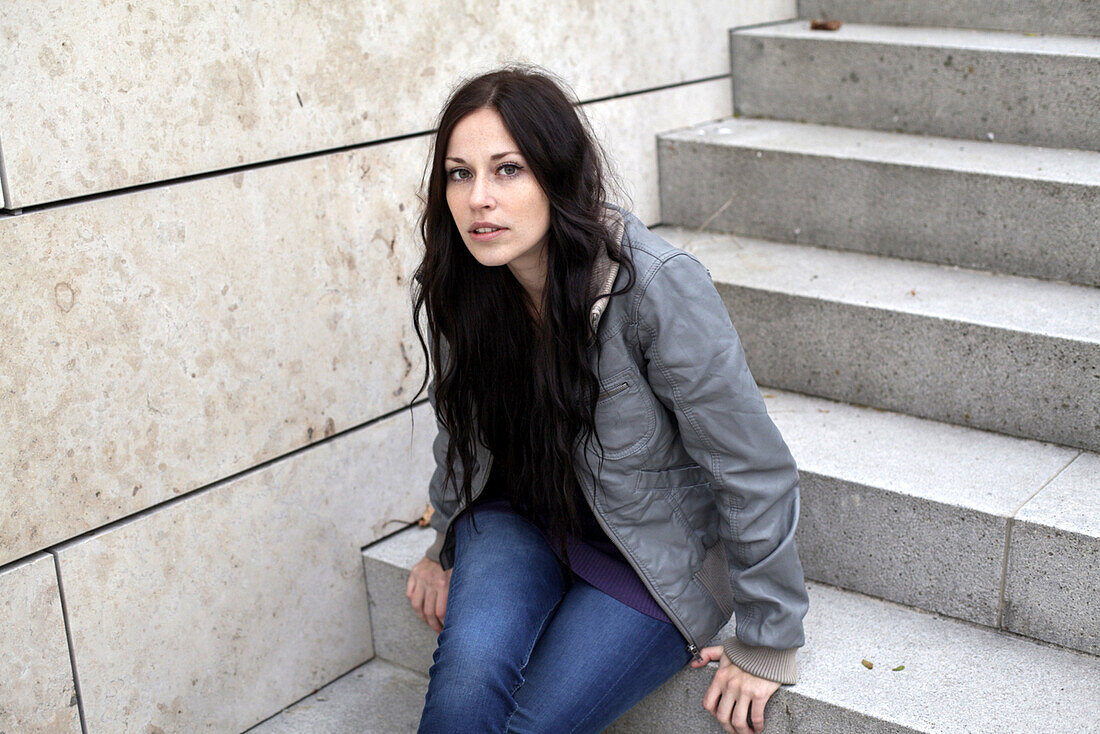 Young woman sitting on a staircase looking at camera, Munich, Bavaria, Germany