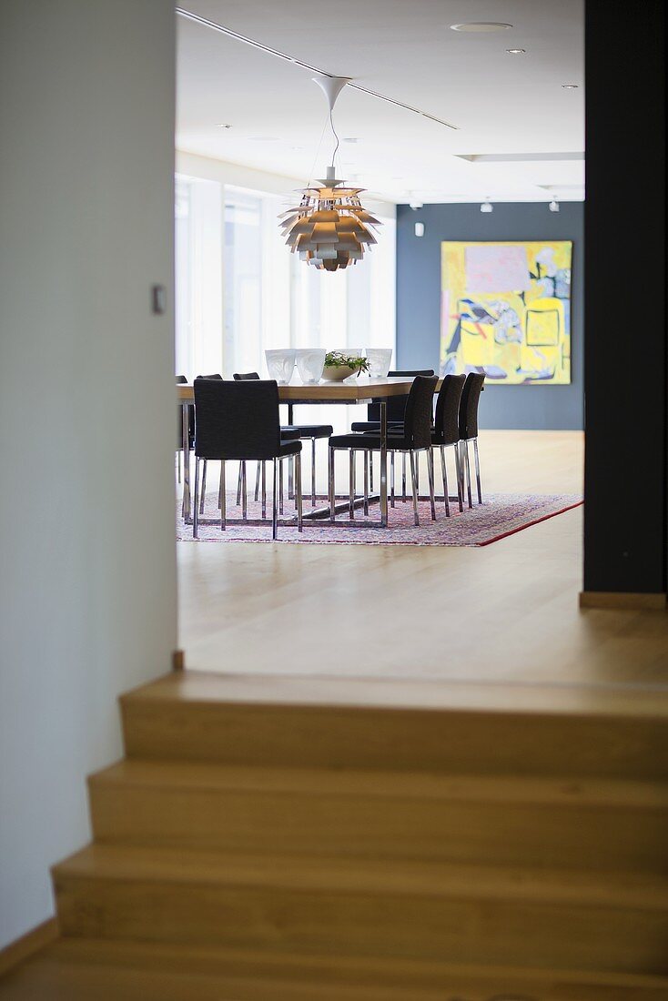 Wooden steps up to a dining room with a designer lamp and a black wall