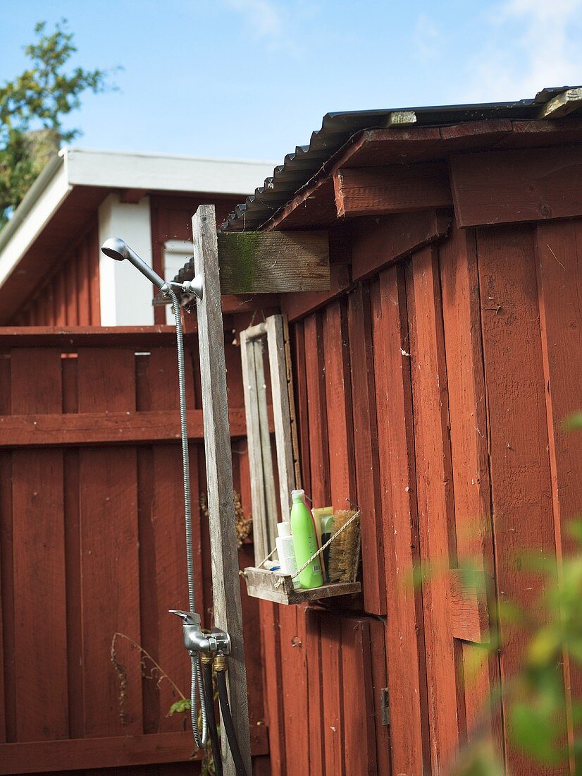 A homemade outdoor shower on a red-painted wooden house