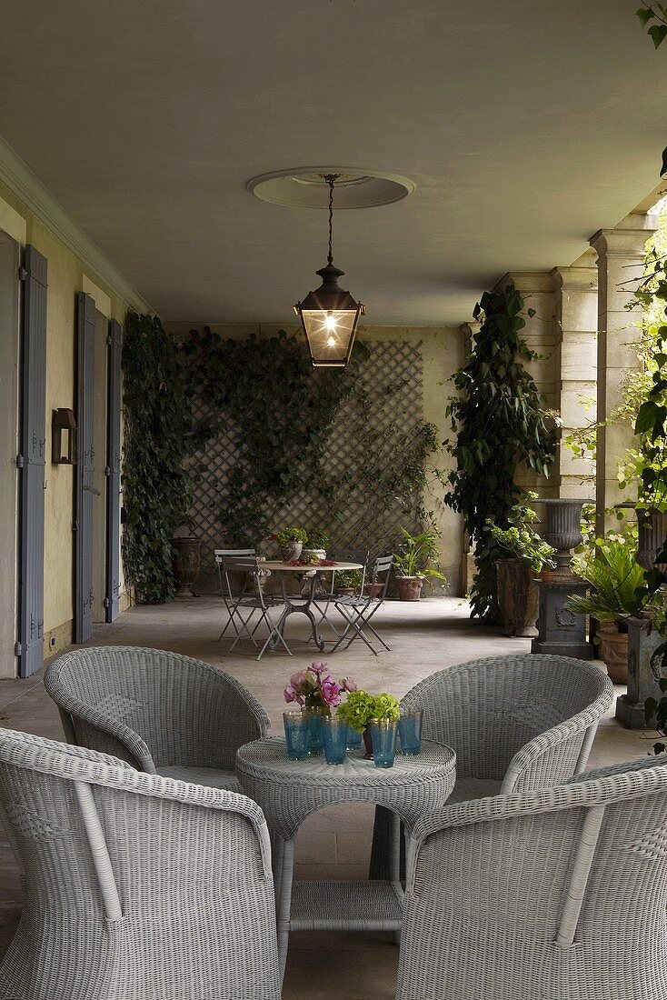 Light gray wicker furniture and planters on the loggia of a villa with lanterns hanging from the ceiling