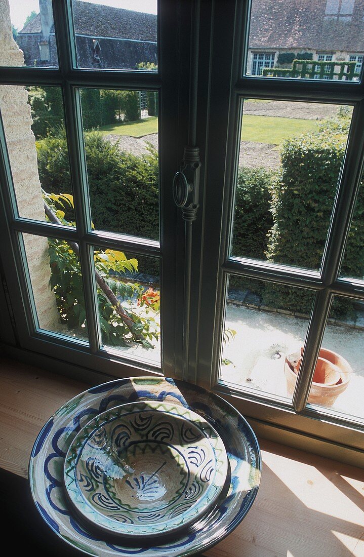 Stacked bowls on a window sill, behind it a view of a garden