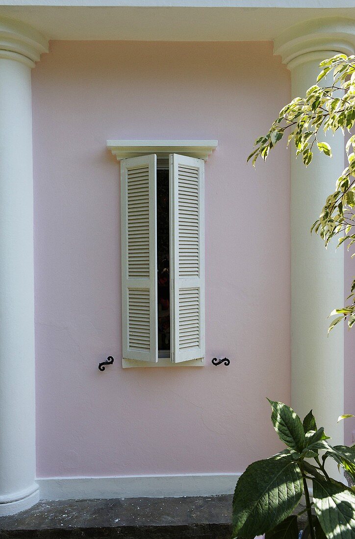 Window with wooden shutters and pink house facade with half columns