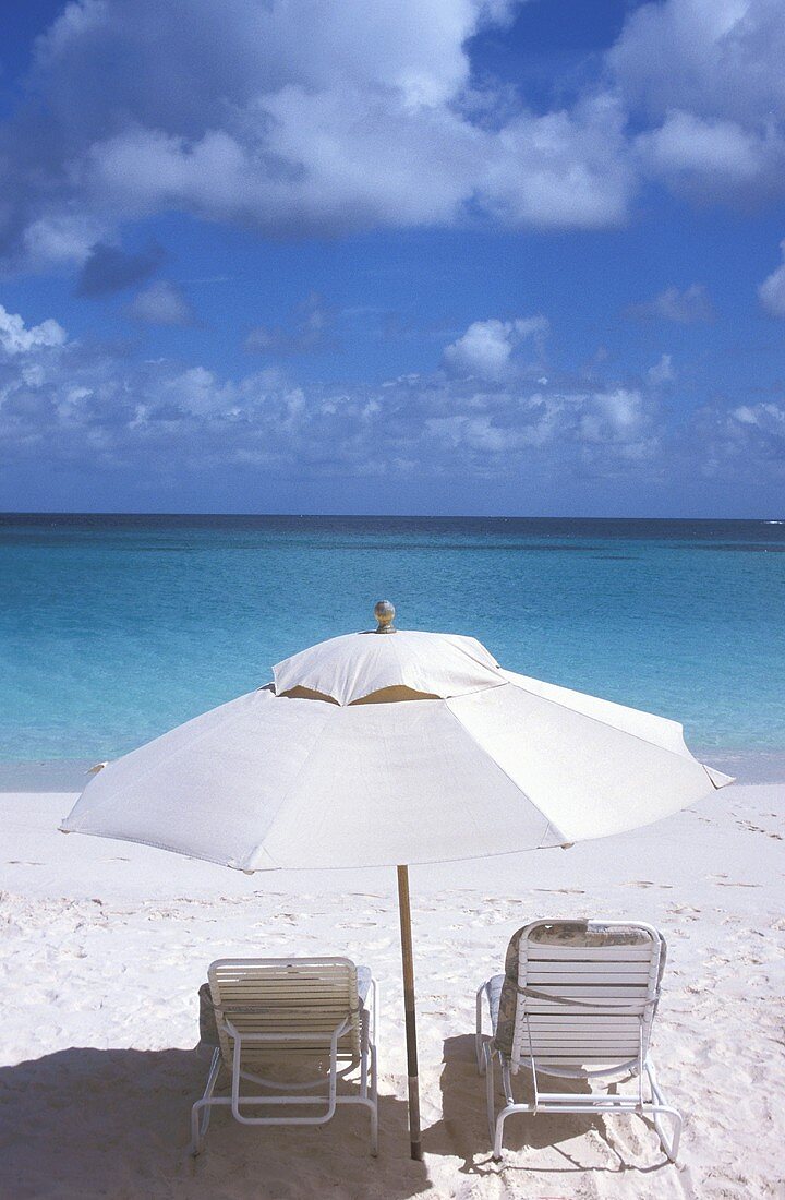 White sand beach, view of the ocean -- lounge chairs under a sun umbrella casting a wide shadow