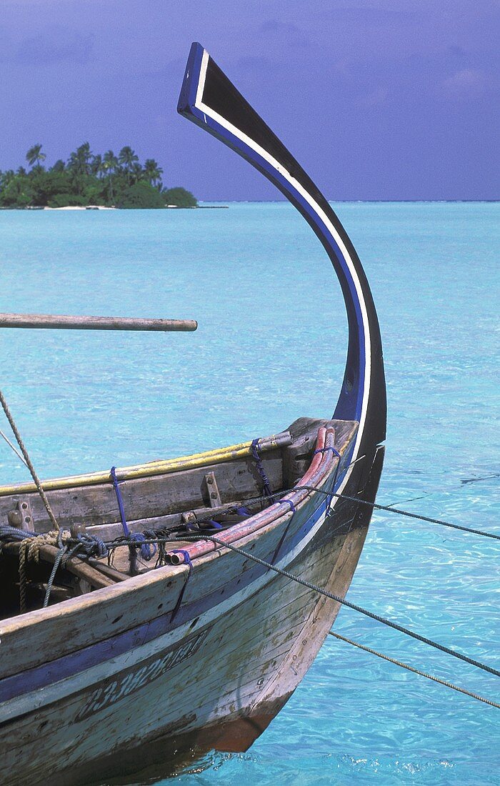 Wooden boat with a curved keel floats in a turquoise sea, in the background a view of an island with a palm forest