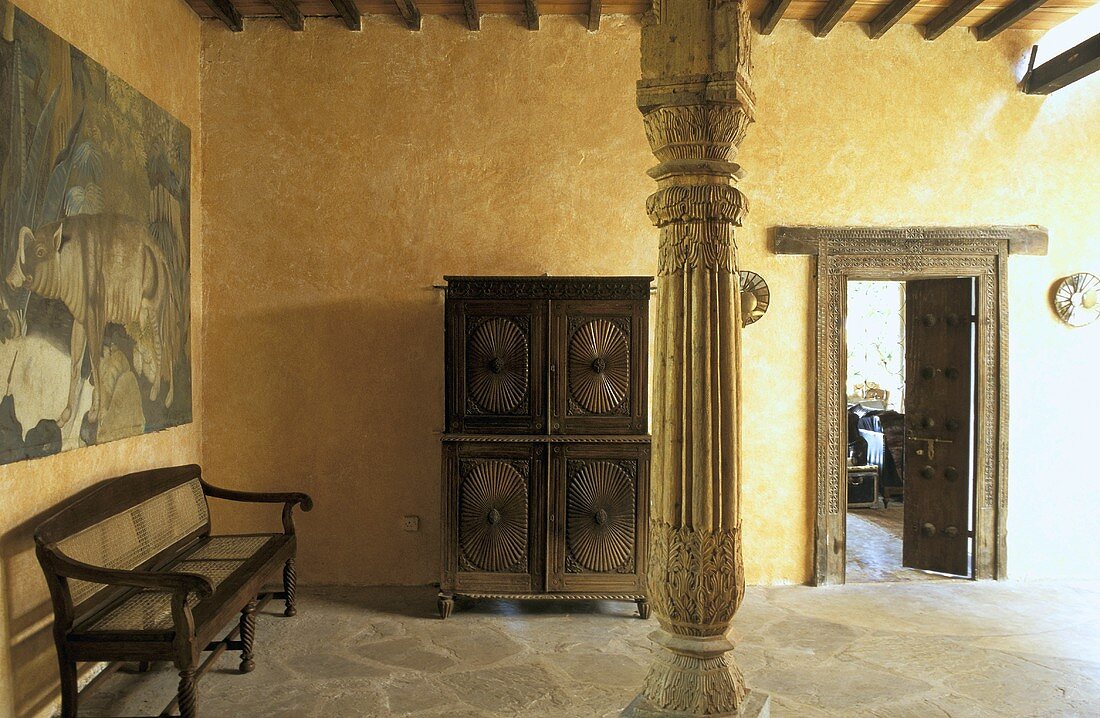 Sparsely furnished room with a yellow wall and carved wooden support in an African house