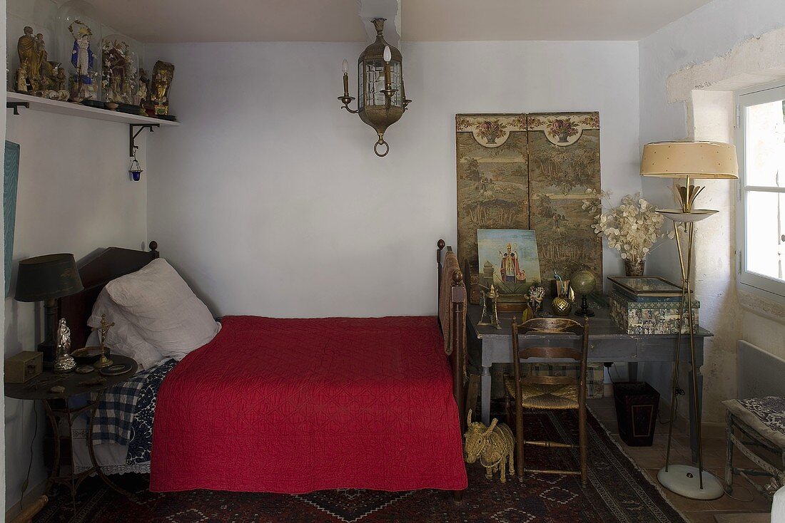 North African style bedroom with a red bedspread and table with floor lamp at the foot of the bed