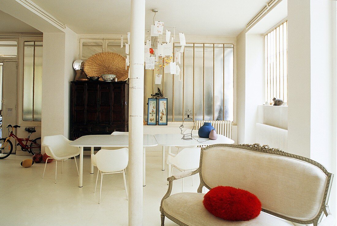 White loft with antique upholstered sofa and red pillow in front of a column and dining area
