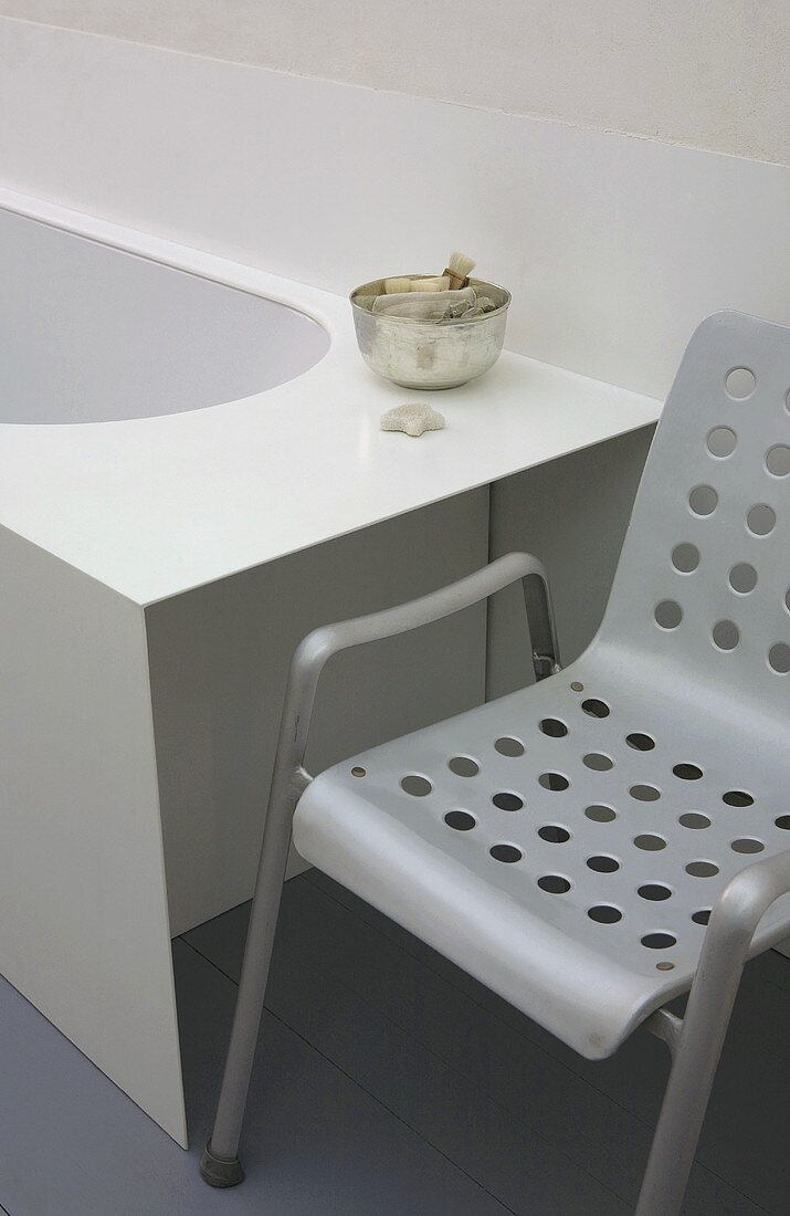 Gray metal chair with holes in the seat and backrest next to a bathtub