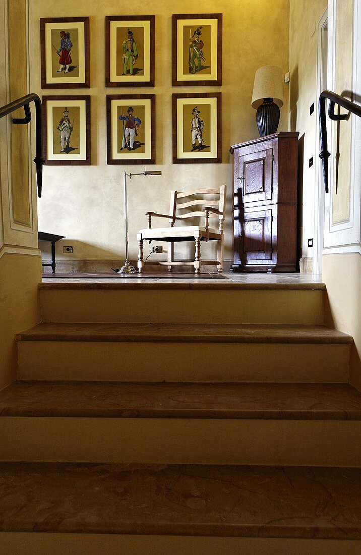 Looking up a stairway with a view of a picture collection and a chair next to a corner cupboard