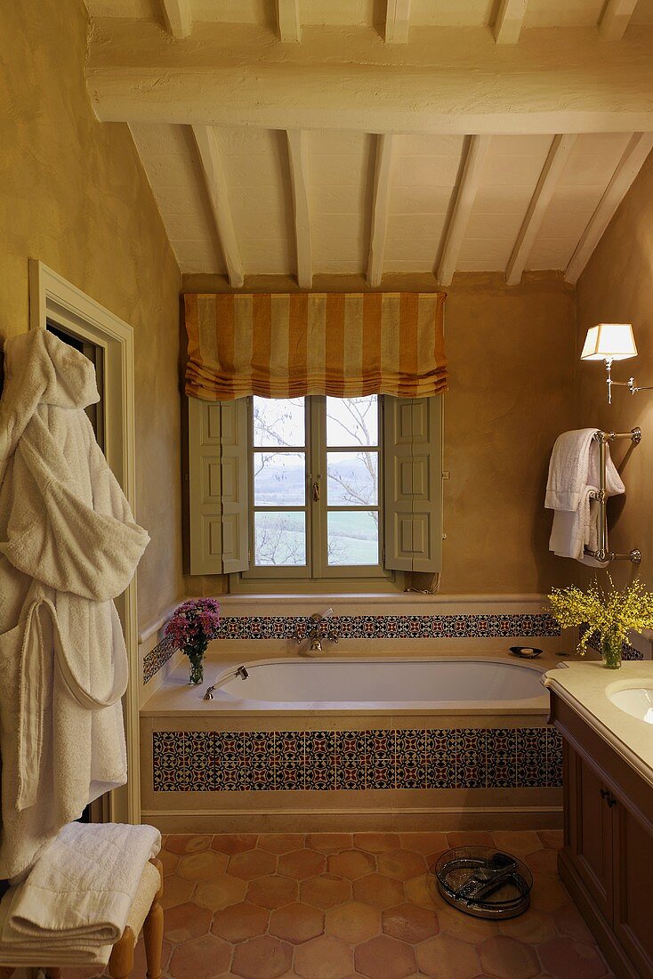 A built in bath tub in front of a window with patterned tiles and wooden ceiling in an attic