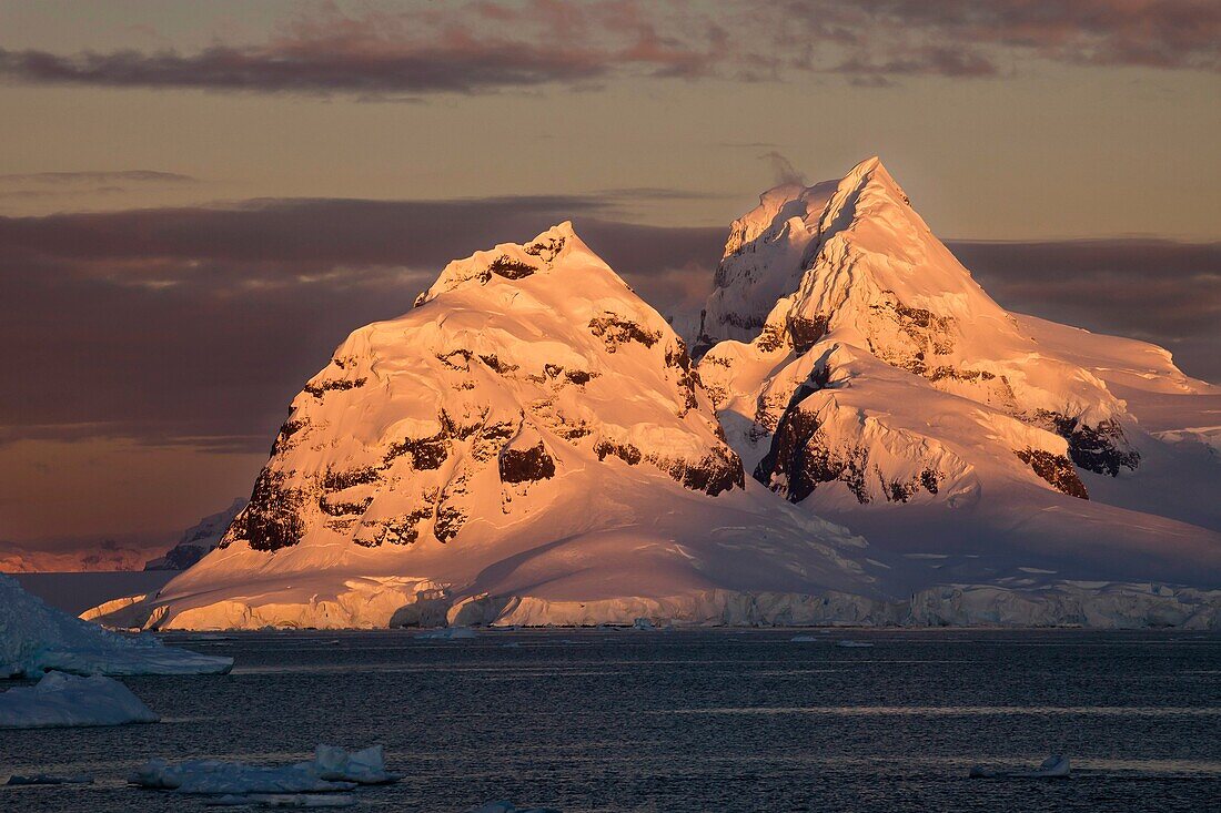 Alpenglow lights up high peaks on Wiencke Island behind Port Lockroy, Antarctic Peninsula.