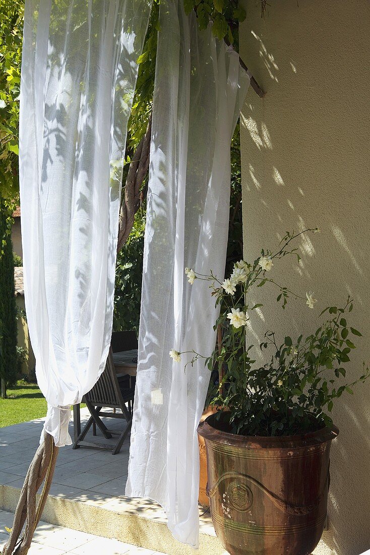 Airy curtains and antique copper planters in front of the corner of a house and terrace