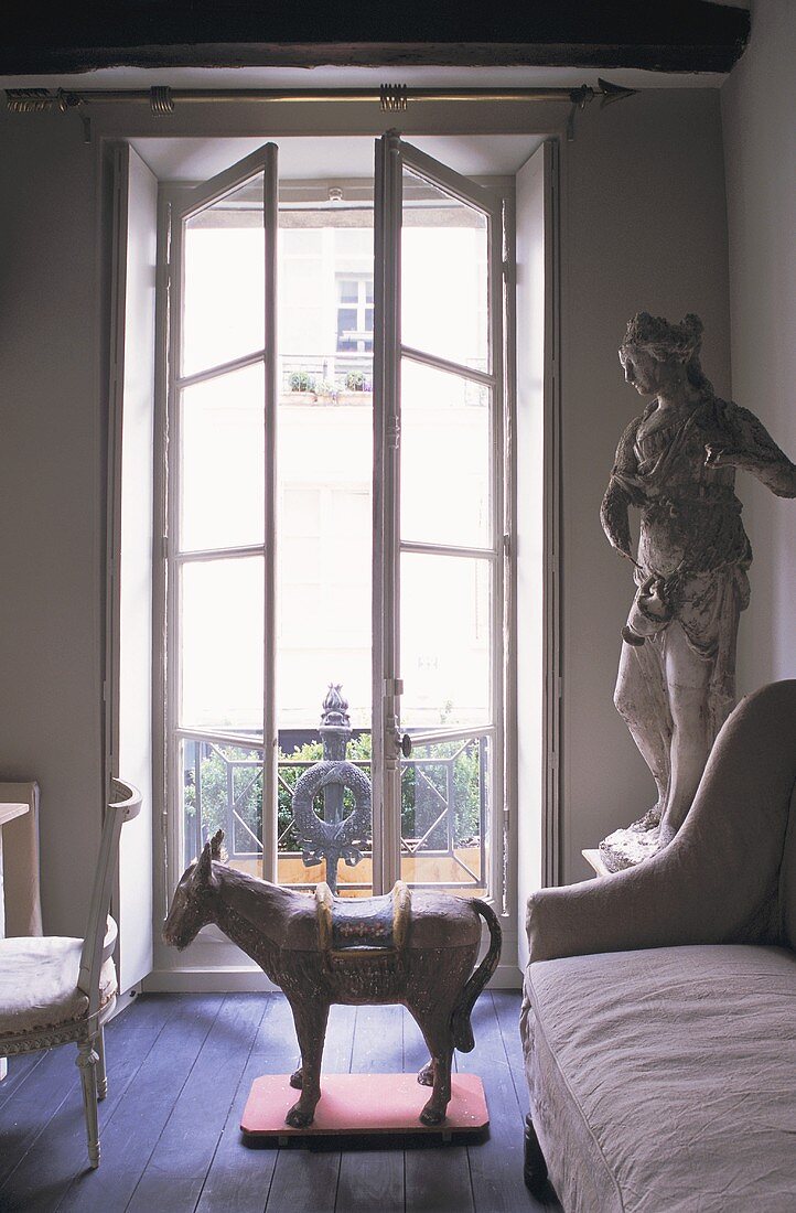 Antike Tierfigur und Steinstatue vor offenstehenden Fenstertüren