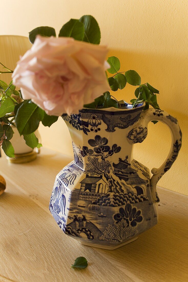 Blooming rose in a painted porcelain vase on a wooden countertop