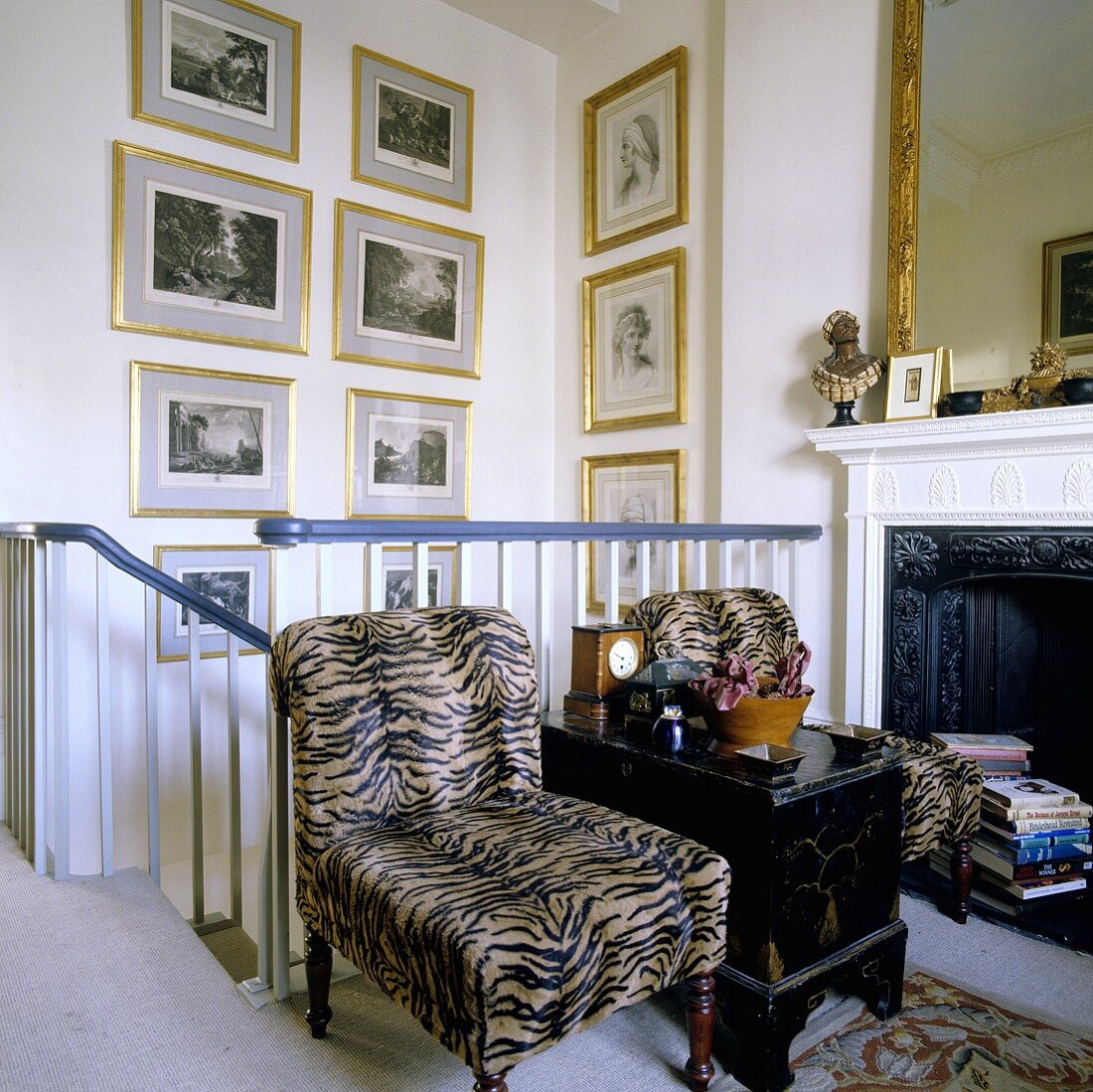 Armchairs with fur covers against a banister rail in front of a fireplace and pictures in gold frames hanging on the wall of the stairwell