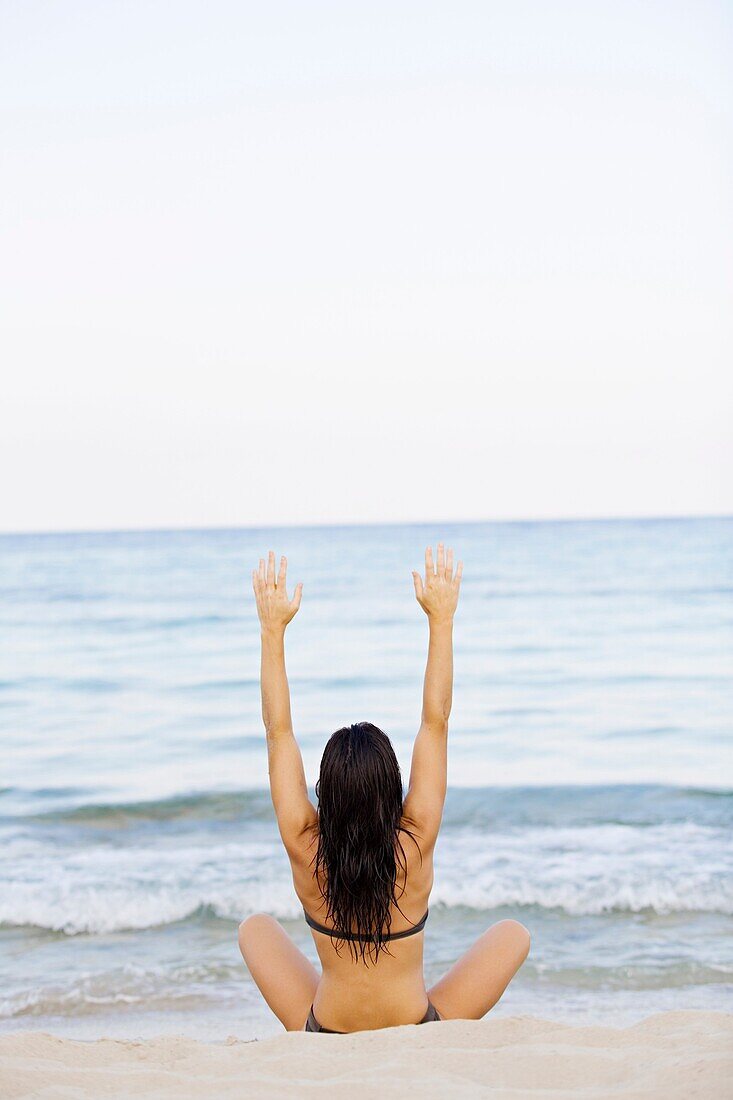 Rückenansicht einer jungen Frau beim Dehnen am Strand