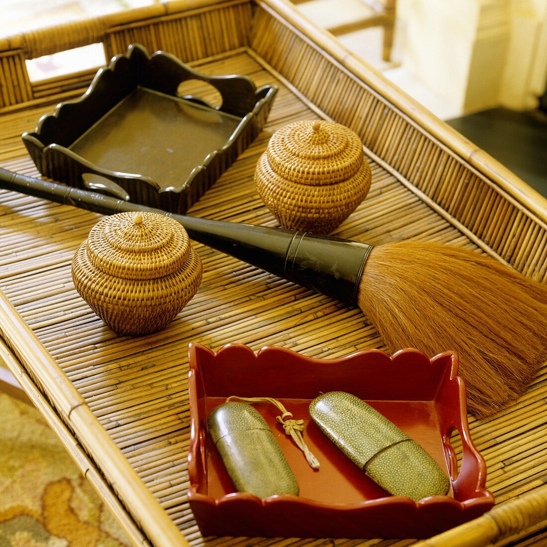 An arrangement on a bamboo tray with a varnished wooden bowl, mini wicker baskets and a bushy brush