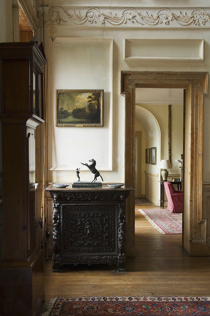 A dark wooden cupboard with carvings next to an open door and a view into the next room